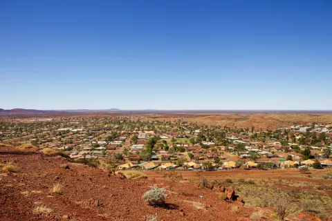Photo of Newman town, in Western Australia. Hundreds of houses are shown against the red Pilbara dirt, under a blue sky